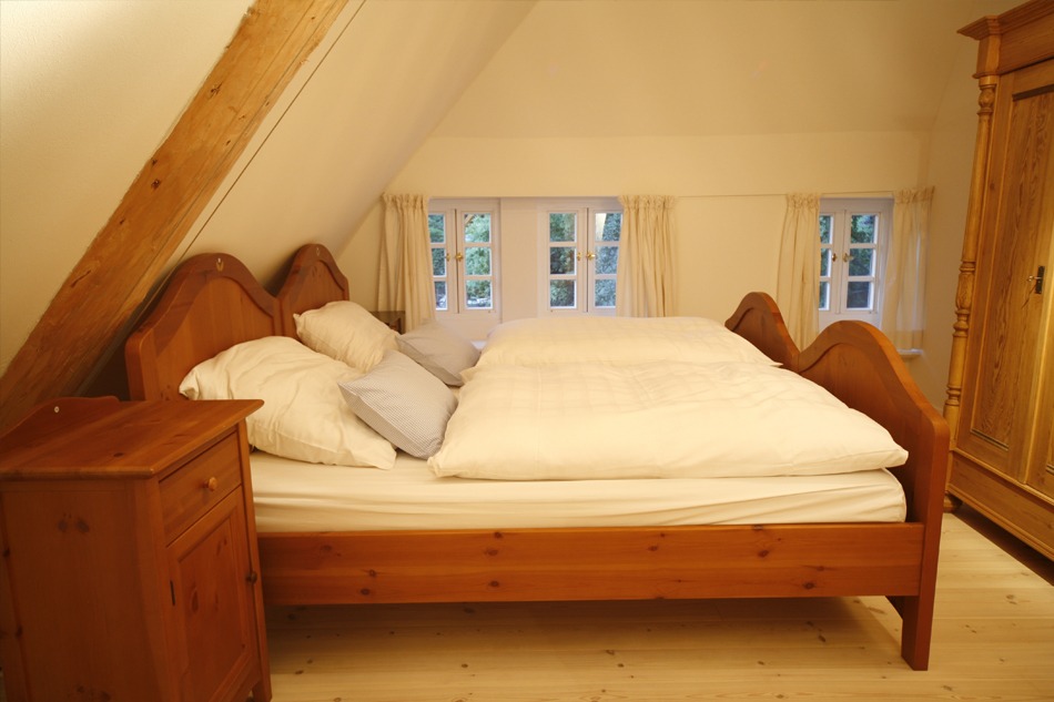 Gemütliches Schlafzimmer im Dachgeschoss mit hölzernem Doppelbett und Bauernkleiderschrank