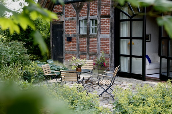 FeWo Harms Hoff – Terrasse Offene Terrasse mit vier Gartenstühlen und Tisch, umgeben von Grün